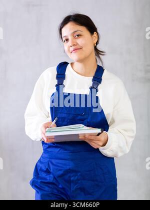 Interessierte Mechanikerin in blauen Overalls, die die Reihenfolge aufschreibt Stockfoto
