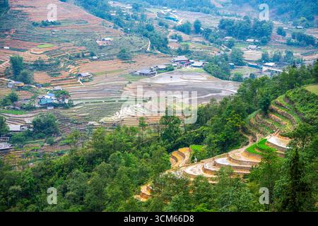 Aus der Vogelperspektive auf Reisterrassen und kleine Dörfer an Berghängen in Sapa, Provinz Lao Cai, Vietnam. Stockfoto