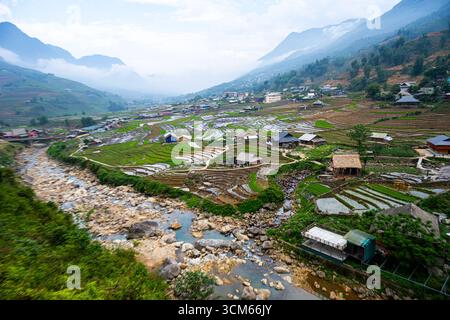 Reisterrassen erstrecken sich entlang eines Flusstals mit verstreuten Häusern im Hochland von Sapa in der Provinz Lao Cai, Vietnam. Stockfoto