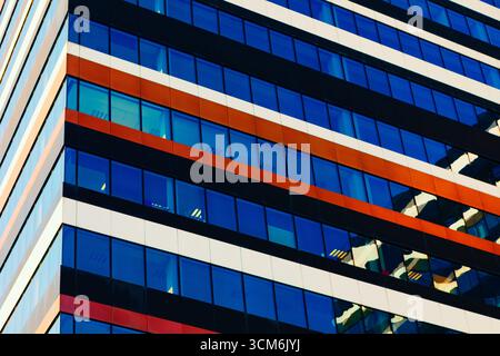 Die elegante Glasfassade eines modernen Bürogebäudes spiegelt dynamische blaue Himmelstöne wider. Geometrische Winkel und lebendige Farben sorgen für ein optisch eindrucksvolles Bild Stockfoto