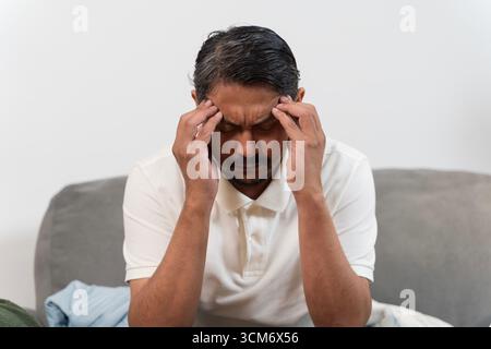 Porträt eines unglücklichen Mannes, der auf dem Sofa sitzt und Schläfen drückt, mit Händen, die Stress und Kopfschmerzen zeigen. Migräne, Müdigkeit, Burnout, Depression, A Stockfoto