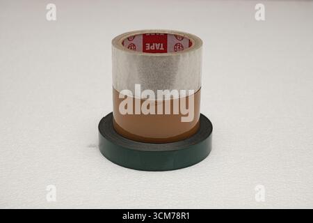Ein Stapel von verschiedenen Rollen Klebeband in verschiedenen Farben, darunter klar, braun und grün, auf einer weißen Oberfläche Stockfoto
