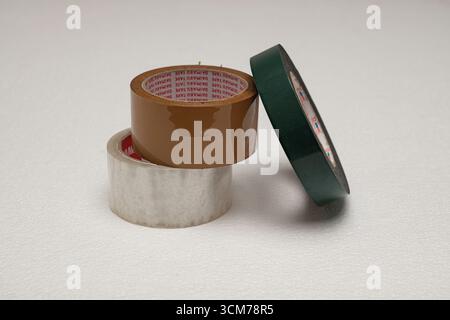 Drei Rollen Klebeband in verschiedenen Farben und Größen, einschließlich braun, grün und klar, auf weißem Hintergrund angeordnet Stockfoto