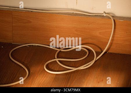 Ein verworrenes weißes Kabel auf einem Holzboden in der Nähe einer Wand Stockfoto