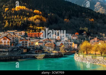Blick auf einen kleinen See und ein Dorf Pietraporzio an den Hängen mit bunten Herbstbäumen im Piemont, Italien. Stockfoto