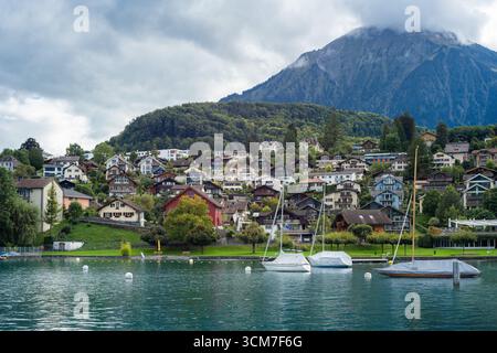 Spiez, Schweiz - 11. September 2025: Ein ruhiger Blick auf den Spiez mit Segelbooten, umgeben von charmanten Häusern und üppigen grünen Hügeln, unter einem C Stockfoto