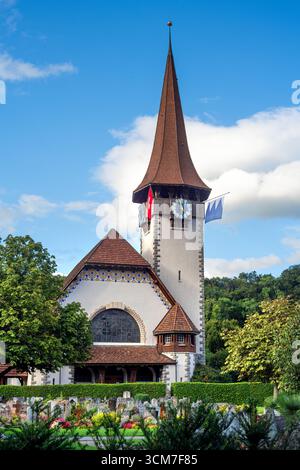 Spiez, Schweiz - 11. September 2025: Eine malerische reformierte Kirche in Spiez mit hohem Turm und Uhr, umgeben von Grün. Stockfoto