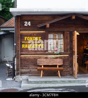 Spiez, Schweiz - 11. September 2025: Ein gemütliches Holzrestaurant mit einem Schild mit FONDUE RACLETTE, einer Bank und dekorativen Pflanzen Stockfoto