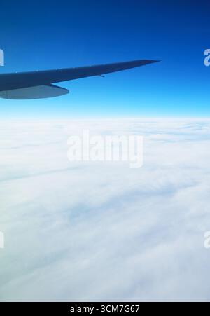 Flugzeugflügel am lebendigen blauen Himmel mit Wolkenmeer Blick vom Flugzeugfenster während des Fluges Stockfoto
