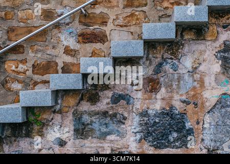 Moderne Graue Steinstufen Gegen Die Alte Verwitterte Wand Mit Architektonischem Kontrast. Moderne Renovierung, historischer Denkmalschutz Stockfoto