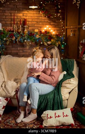 Eine liebevolle Mutter und ihre Tochter küssen sich auf einer gemütlichen Couch, umgeben von festlicher Weihnachtsdekoration. Dieses Bild fängt das intime, zarte e ein Stockfoto