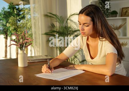 Hausmieter füllen das Formular bei Sonnenuntergang auf einem Holztisch zu Hause aus Stockfoto