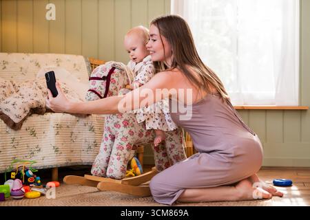 Mom macht ein Selfie mit ihrem Baby, das auf einem Schaukelpferd sitzt Stockfoto