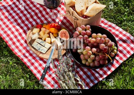 Picknick mit Käse, Obst, Brot und Rotwein auf einer rot-weiß karierten Tischdecke. Draufsicht, Nahaufnahme 2. Stockfoto