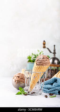 Schokoladeneiskegel mit Waffelstruktur, in eine Glasschale neben frischen Minzblättern und einem gemütlichen blauen Tuch gelegt, Telefonhintergrund mit Kopie s Stockfoto