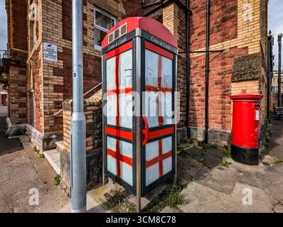 Paignton, Großbritannien. September 2025. Traditionelle rote Telefonbox mit Fenstern, die mit Graffiti der rot-weißen Flagge von St. George, der Nationalflagge Englands, bedeckt sind. Autor: Thomas Faull/Alamy Live News Stockfoto