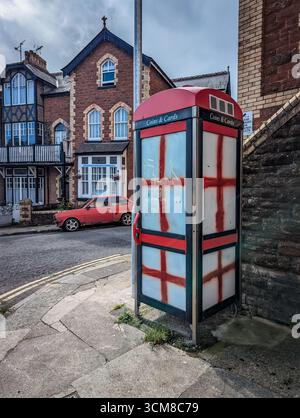 Paignton, Großbritannien. September 2025. Traditionelle rote Telefonbox mit Fenstern, die mit Graffiti der rot-weißen Flagge von St. George, der Nationalflagge Englands, bedeckt sind. Autor: Thomas Faull/Alamy Live News Stockfoto