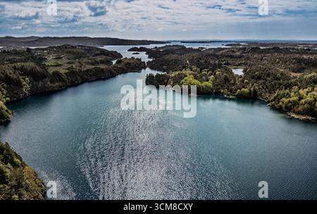 Ein atemberaubender Blick aus der Luft auf eine ruhige Küstenlandschaft mit ruhigem Wasser, umgeben von üppigem Grün, unter einem leicht bewölkten Himmel, was einen schafft Stockfoto