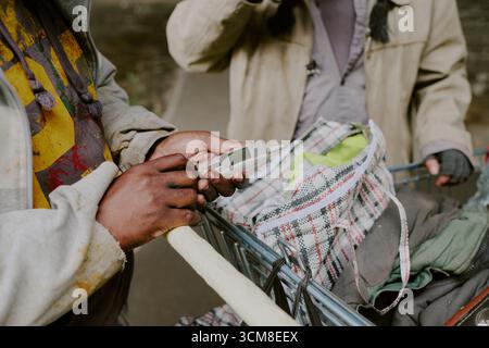 Obdachloser schwarzer Mann, der altes Handy in der Nähe des Einkaufswagens hält Stockfoto