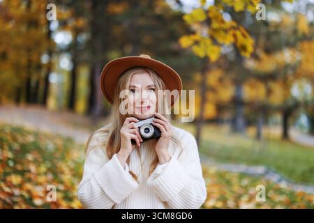 Glückliche Fotografin im Hut mit Retro-Kamera, Herbstleben und Kreativität. Stockfoto