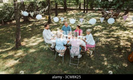 Toller Blick auf Großeltern, Eltern und Kinder, die zusammen draußen essen, am Wochenende Grillparty. Stockfoto
