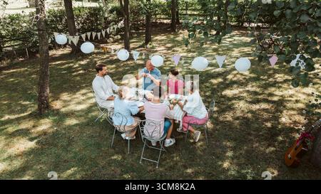 Toller Blick auf Großeltern, Eltern und Kinder, die zusammen draußen essen, am Wochenende Grillparty. Stockfoto