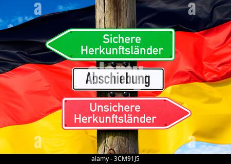 Wegweiser mit Abschiebung, sicheren Herkunftsländern und unsicheren Herkunftsländern vor der deutschen Flagge, Fotomontage Stockfoto
