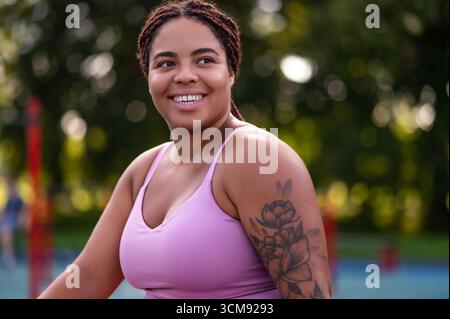 Frau in Übergröße mit geflochtenen Haaren im Sportoutfit, die zur Seite blickt Stockfoto