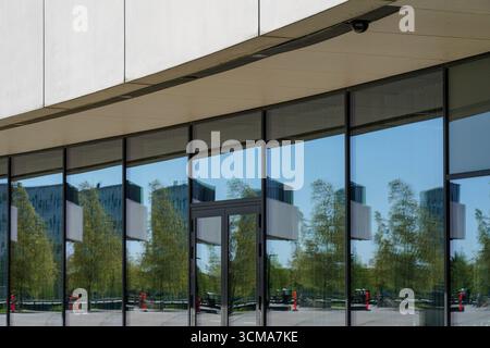 Dänemark, Kopenhagen. Die Royal Arena verfügt über verspiegelte Glaspaneele, die die Bewegung und das Licht der Stadt widerspiegeln. Wechselnde Reflexionen von Gebäuden, Bäumen und Jahreszeiten verwandeln die Fassade in eine dynamische urbane Symphonie. Stockfoto