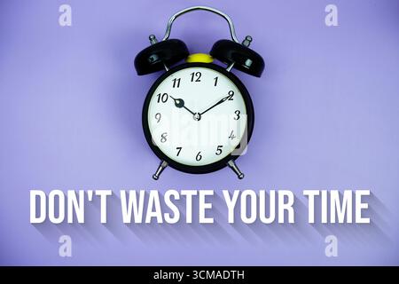 Verschwenden Sie Ihre Zeit nicht mit Text und Wecker auf violettem Hintergrund Stockfoto