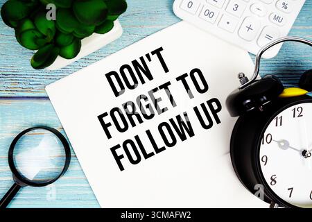 Vergessen Sie nicht, auf Papier zu schreiben, das auf einer blauen Holzoberfläche neben einer Lupe, einer Uhr, einem Taschenrechner und einer kleinen Pflanze liegt Stockfoto