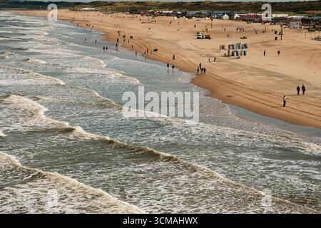 Strand Küste Wellen Menschen Sand Küste. Breiter Sandstrand mit sanften Wellen und verstreuten Menschen, die entlang der Küste spazieren, schaffen entspanntes Meer Stockfoto