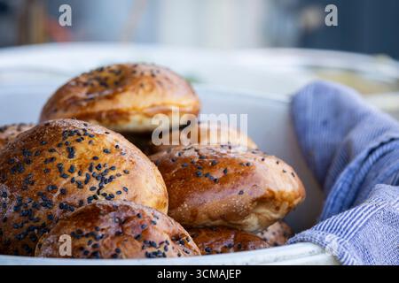 Hamburger Brötchen mit schwarzen Sesamsamen. Runde Sandwichbrötchen mit schwarzem Sesam. Hausgemachtes Brötchen für Burger in Schüssel. Stockfoto