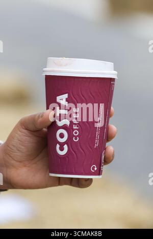 Costa Coffee Tasse mit Lippenstift in einer Hand. Nahaufnahme und isoliert vor einem unscharfen Hintergrund Stockfoto