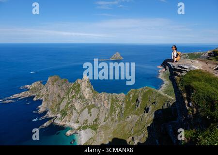 Erleben Sie das atemberaubende Panorama vom Berg Matind in Andoya, Norwegen. Ein einsamer Wanderer genießt die unberührte Aussicht auf die dramatischen Klippen und das glitzernde blaue Meer darunter. Stockfoto