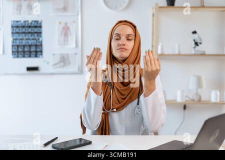 Junge muslimische Ärztin, die im Krankenhaus arbeitet, entspannen sich mit geschlossenen Augen während der Meditation. Kopierbereich Stockfoto