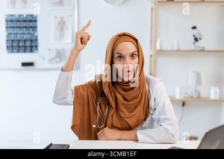 Junge muslimische Ärztin mit Stethoskop, der den Finger nach oben zeigt. Konzept von Medizin und Gesundheitswesen Stockfoto