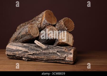 Haufen von geschnittenem Brennholz auf Holztisch vor braunem Hintergrund, Nahaufnahme Stockfoto