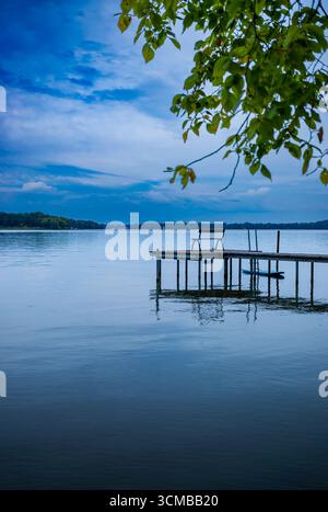Eine einsame Bank sitzt auf einem schmalen Dock über der ruhigen Havel bei Caputh, Brandenburg, unter einem stimmungsvollen Herbsthimmel (senkrecht). Stockfoto