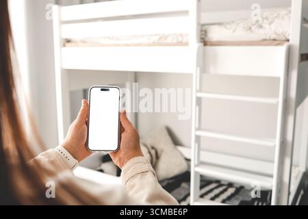 Telefon mit isoliertem Bildschirm im Kinderzimmer vor dem Hintergrund eines Stockbetts, Möbel bestellen. Stockfoto
