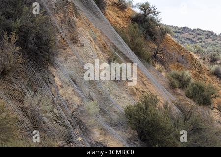 Ein Stahlnetz bedeckt einen steilen Hang, um Fahrer auf der darunter liegenden Fahrbahn vor herabfallenden Felsen zu schützen. Stockfoto