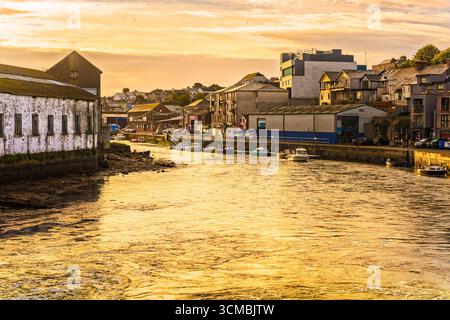 Goldenes Licht über Wicklow Harbour und Vartry River mit vertäuten Booten, Steinbrücke und Gebäuden am Fluss. Stockfoto