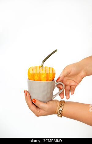 Frauenhände, die Kürbis und eine Tasse heißes Getränk auf weißem Hintergrund halten Stockfoto