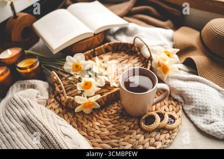 Stillleben im Frühling, Tasse Tee, Kerzen, offenes Buch und Hut. Stockfoto
