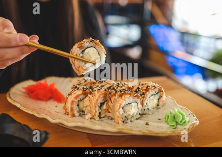 Schöne junge Frau, die Sushi-Rolle im Café isst. Frau, die Sushi mit Essstäbchen im Restaurant isst. Stockfoto