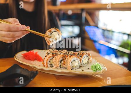 Schöne junge Frau, die Sushi-Rolle im Café isst. Frau, die Sushi mit Essstäbchen im Restaurant isst. Stockfoto