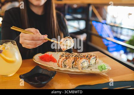 Schöne junge Frau, die Sushi-Rolle im Café isst. Frau, die Sushi mit Essstäbchen im Restaurant isst. Stockfoto