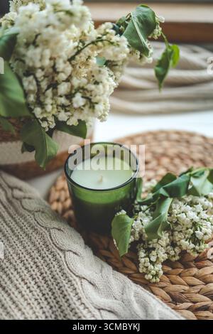 Kerze in einem grünen Glas, ein offenes Buch und ein Blumenstrauß aus weißem Flieder, Frühlingsinnenraum. Stockfoto