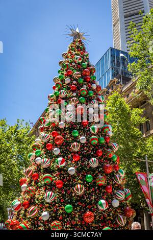Ein großer, aufwendig verzierter Weihnachtsbaum steht in Sydney, Australien, vor dem Hintergrund des blauen Himmels und der nahe gelegenen Gebäude. Stockfoto