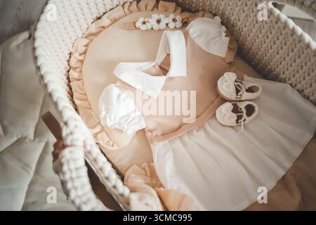 Babykleidung und Accessoires, Kleid und handgefertigte Strickschuhe in der Wiege. Modeartikel für Neugeborene, Draufsicht. Stockfoto